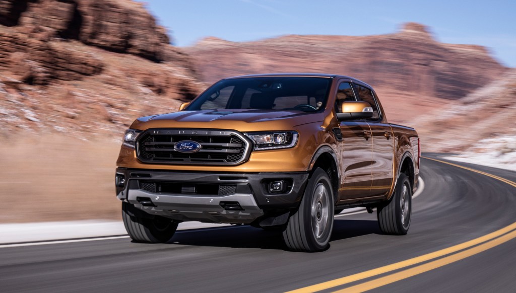 An orange 2019 Ford Ranger pickup truck at speed on a road with a mountain background