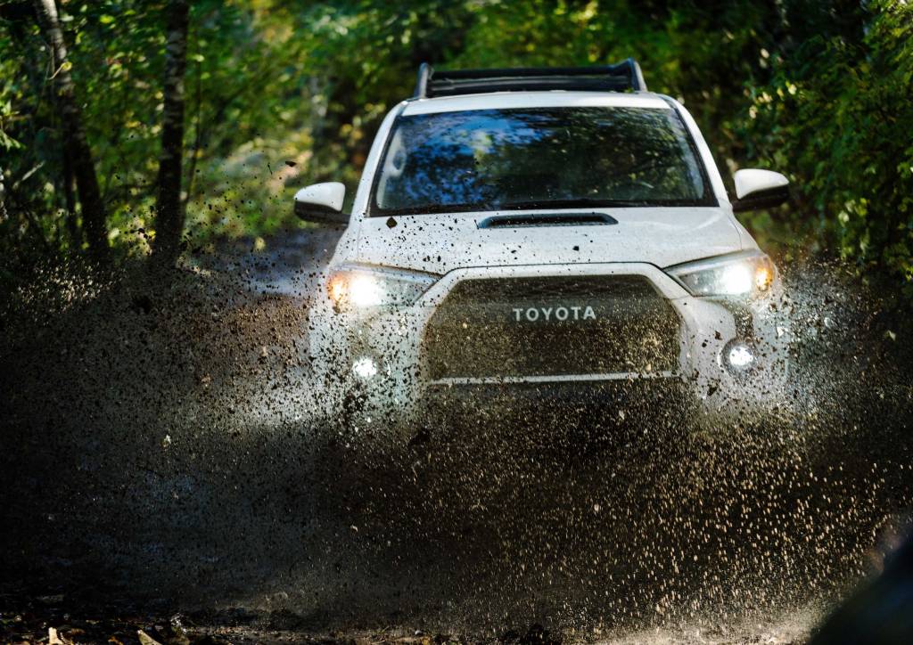 a white off-riding TRD Pro trim Toyota 4Runner splashes through the mud on an off-road trail in the woods
