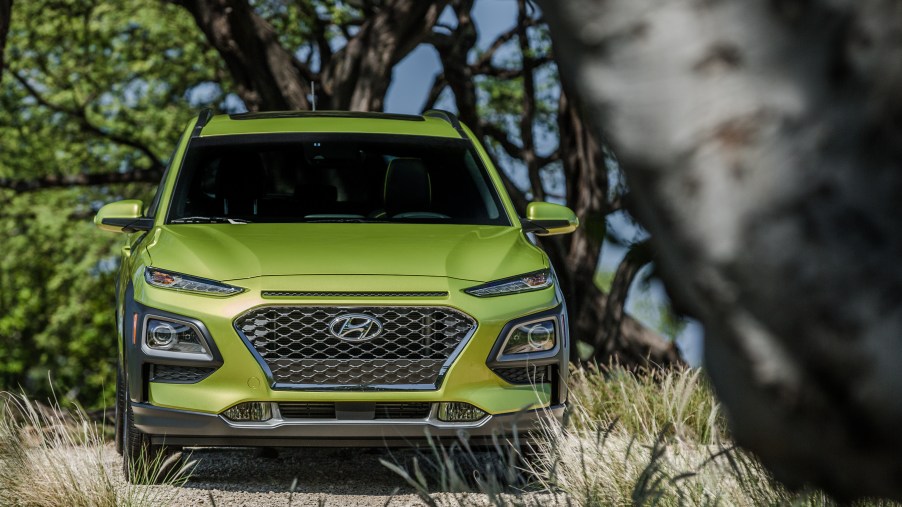 a bright green Hyundai Kona crossover SUV rests in a heavily treed parking lot