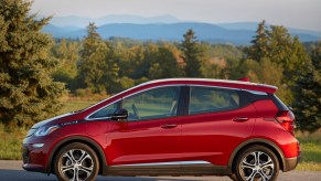 A red Chevy bolt parked before trees and a mountain