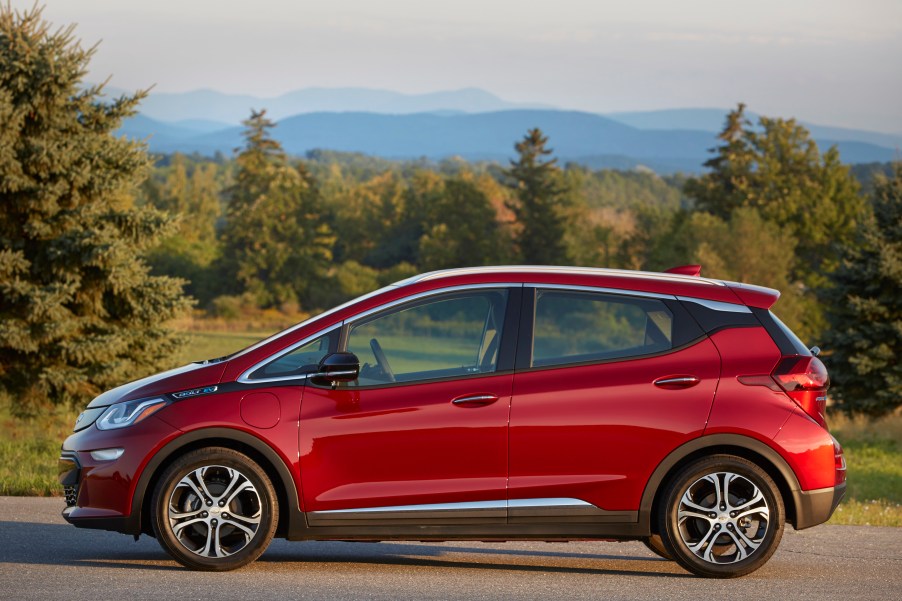 A red Chevy bolt parked before trees and a mountain