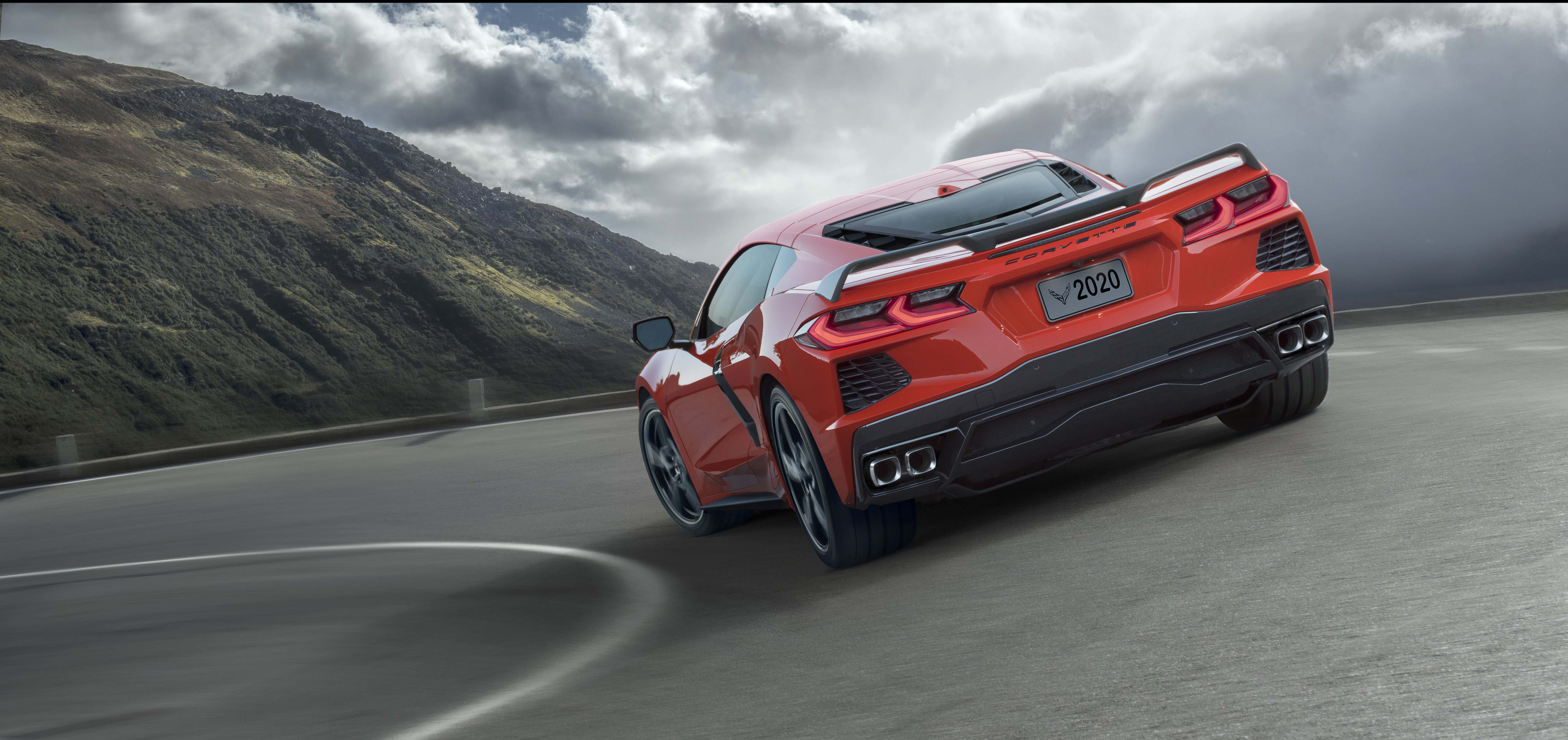 A red Corvette rounds a turn on a mountain pass.