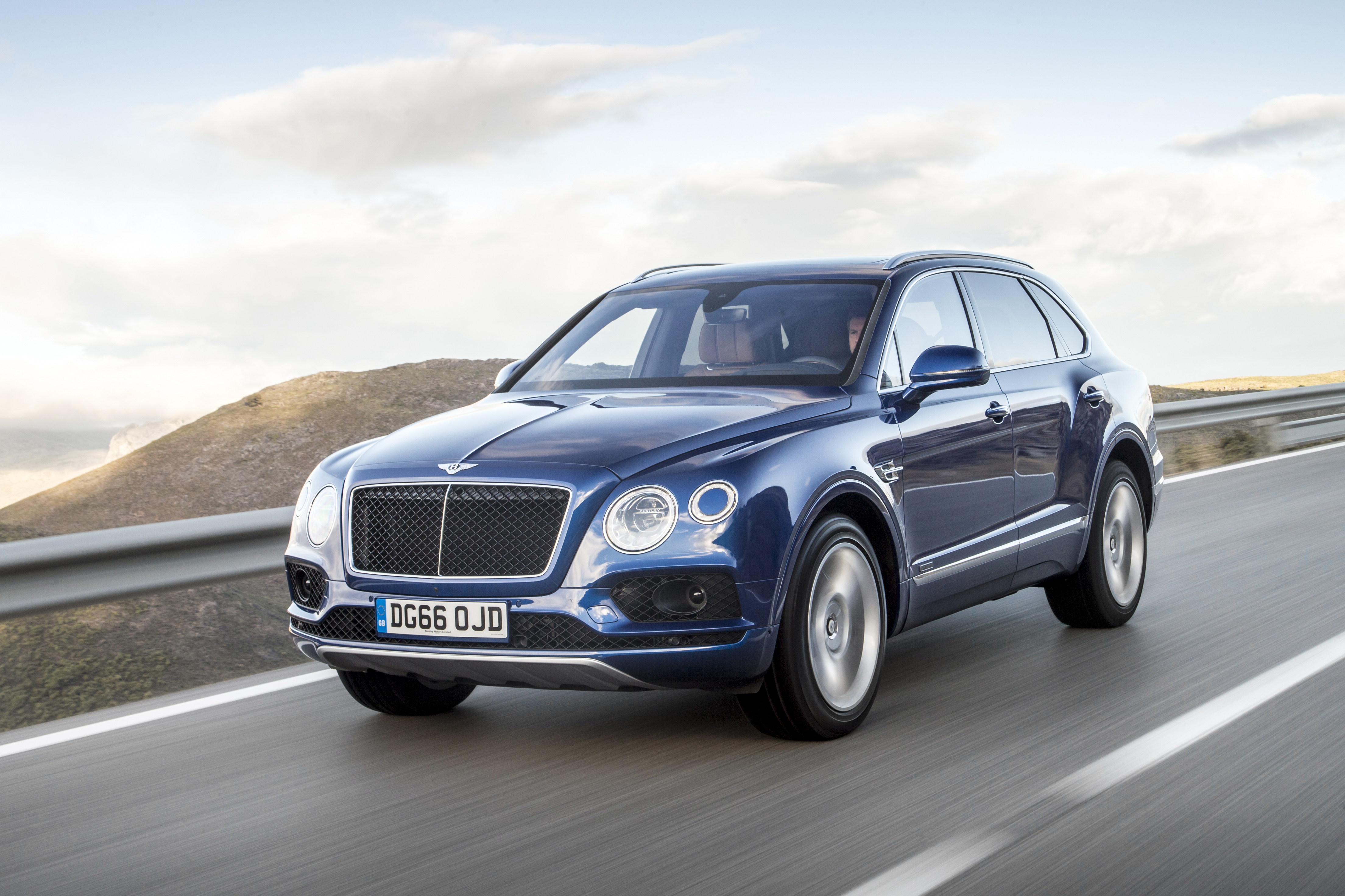 a blue Bentley Bentayga SUV at speed on a scenic road