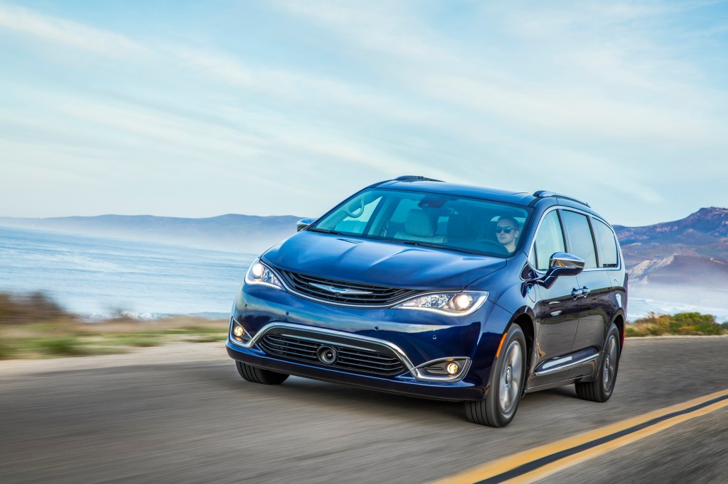  a dark blue Chrysler Pacifica hybrid at speed on a scenic road is one example of brands competing in the hybrid segment