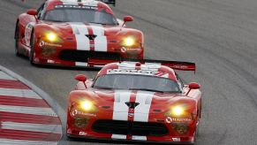 Two red Dodge Vipers with white racing stripes race around a track