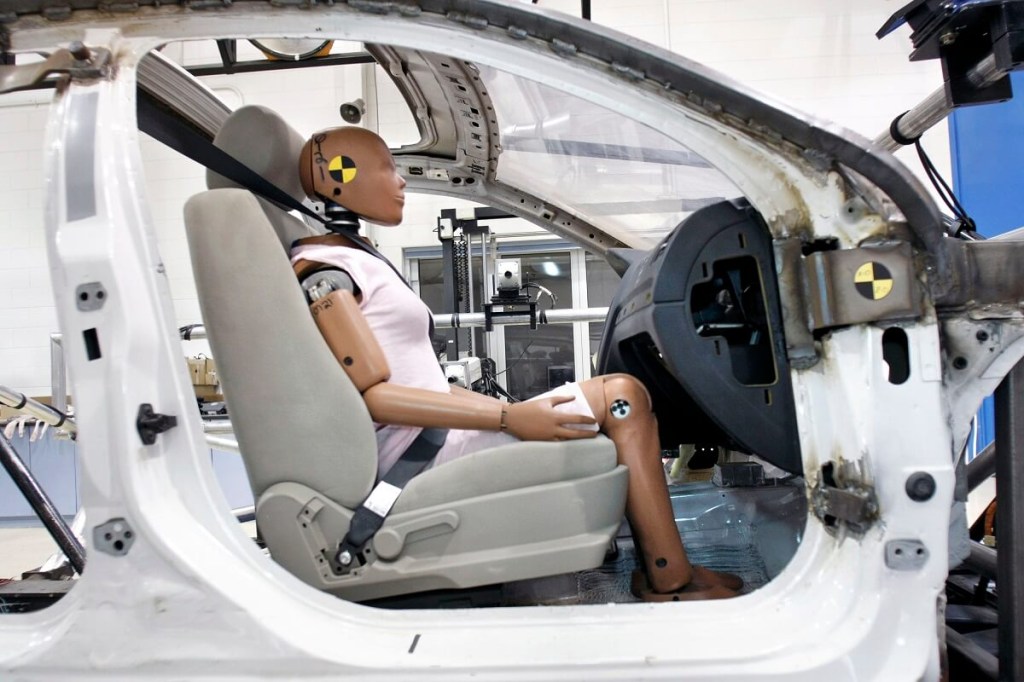A test dummy for crash rating determinations for the NHTSA or IIHS sits in a vehicle cabin. 