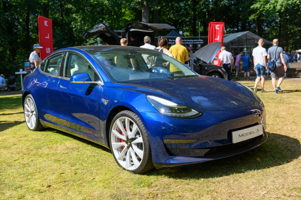 A blue Tesla Model 3 is a displayed at a car event