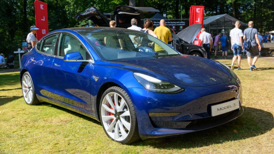 A blue Tesla Model 3 is a displayed at a car event