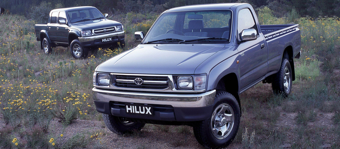 single and double cab models of the 1998 Toyota Hilux on display together in a field of yellow wildflowers.
