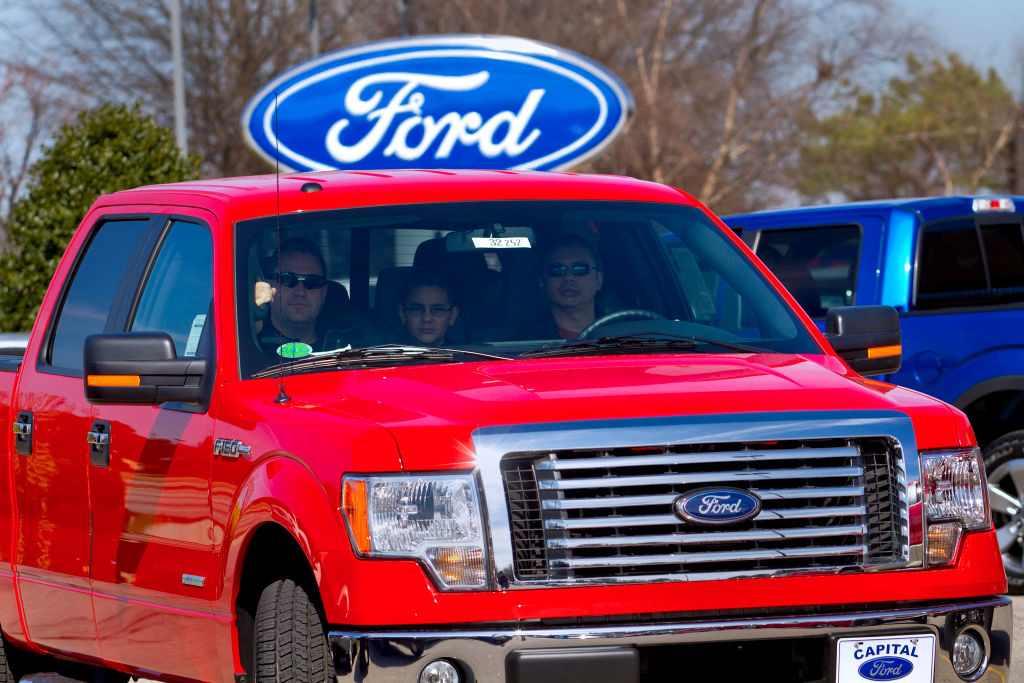 A red 2012 Ford F-150 driving off the car lot.