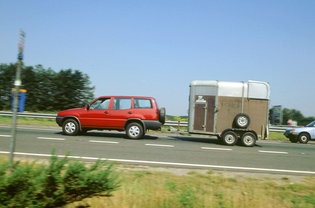 A red SUV towing a small trailer along a road