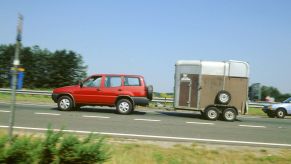 A red SUV towing a small trailer along a road