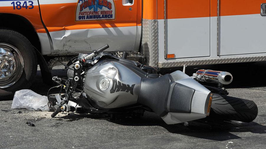A crashed motorcycle lays in front of an ambulance