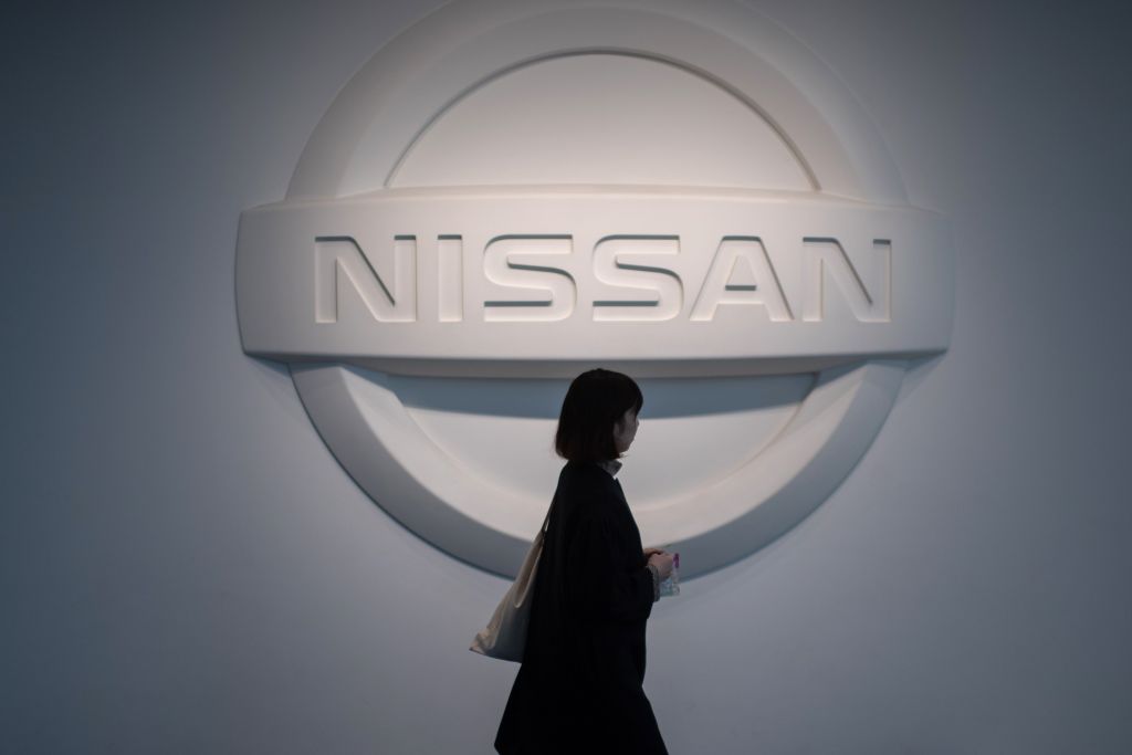 Woman walking by a big Nissan logo on the wall.