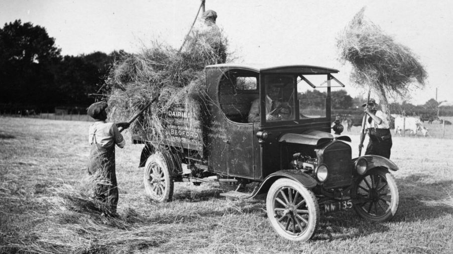 Men loading hay into the back of the back of an old pickup truck.