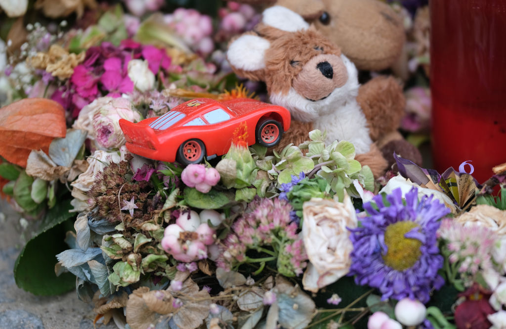 A toy car lies among flowers and candles left by mourners at the site of a pedestrian accident