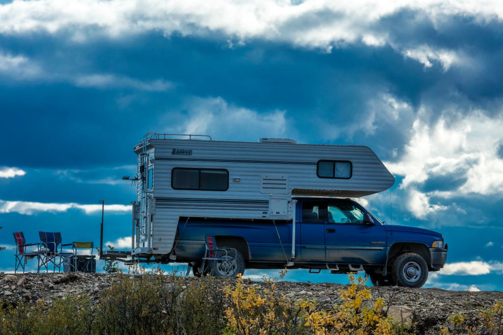 An older pickup truck with a camper in the bed parked on a road.