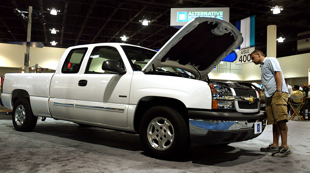 A person inspecting the engine on a pickup truck at an auto show.