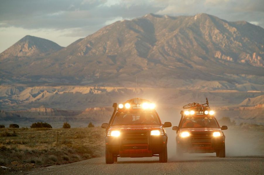 Two off-road trucks with light bars drive down a highway.