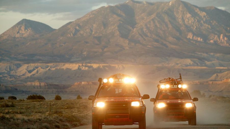 Two off-road trucks with light bars drive down a highway.