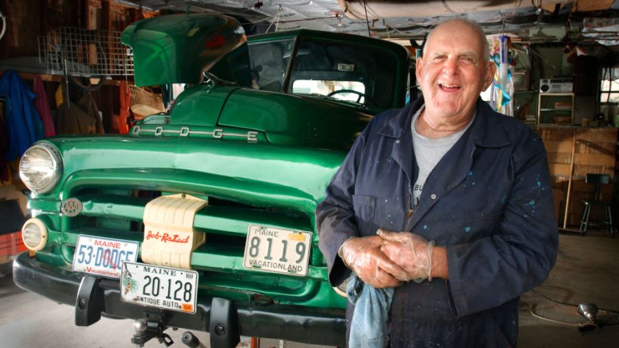 An older man standing next to a truck that he is restoring.