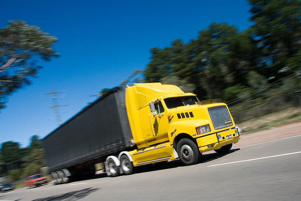 A yellow freight truck speeds down an empty road