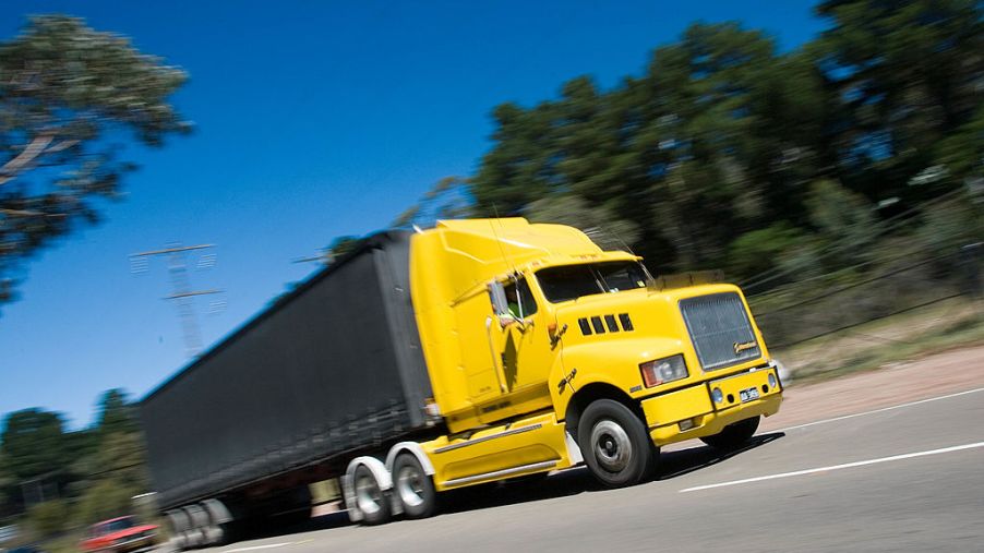 A yellow freight truck speeds down an empty road