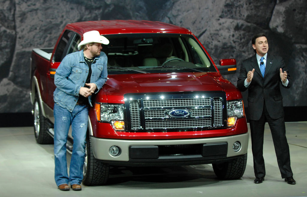 Two people showing off a Ford F-150 at an auto show.