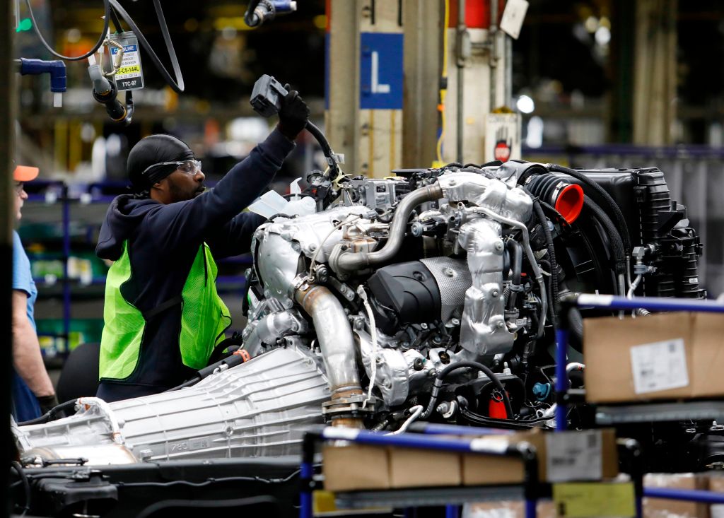 Workers help assemble an engine at a GM plant.