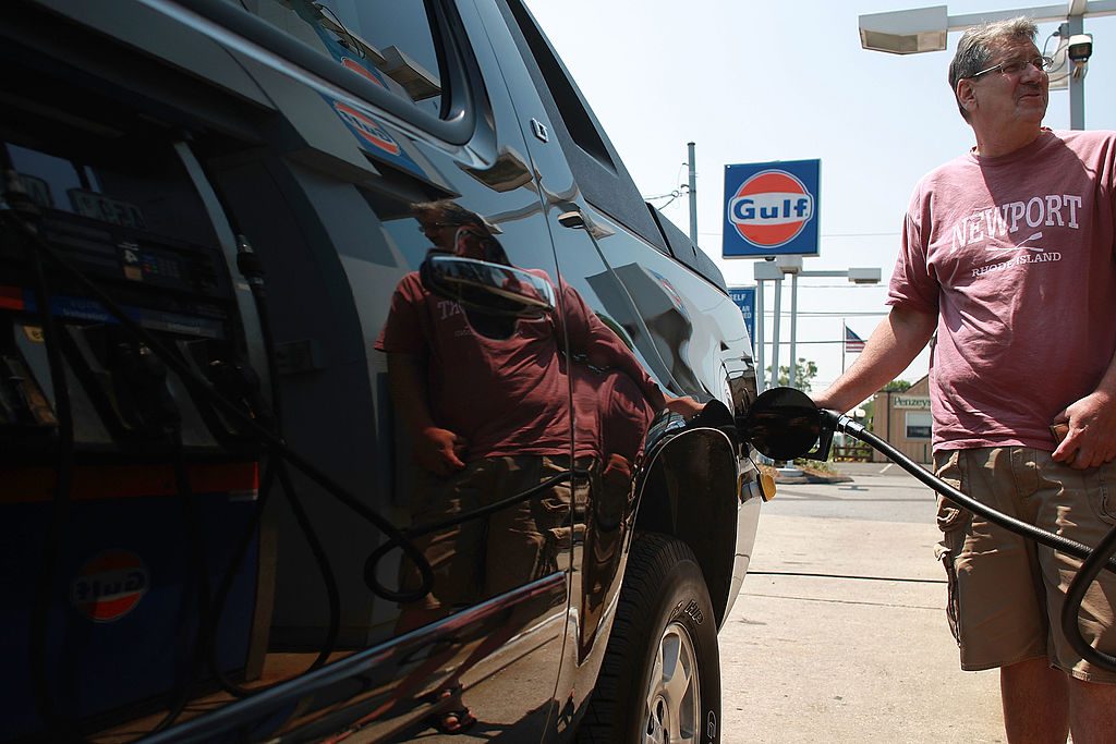 A man stands at a fuel pump to fill up his pickup truck.