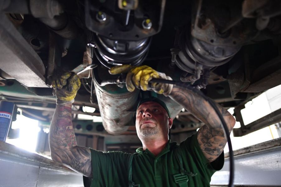 A truck mechanic works on the underside of a diesel truck