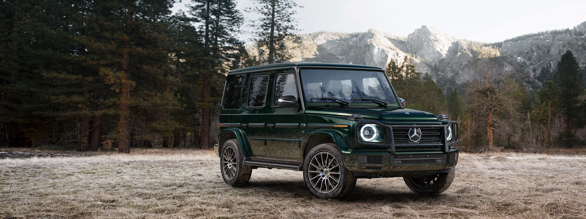 a Mercedes-Benz G-Class Wagen SUV parked in a clearing in the mountains. 