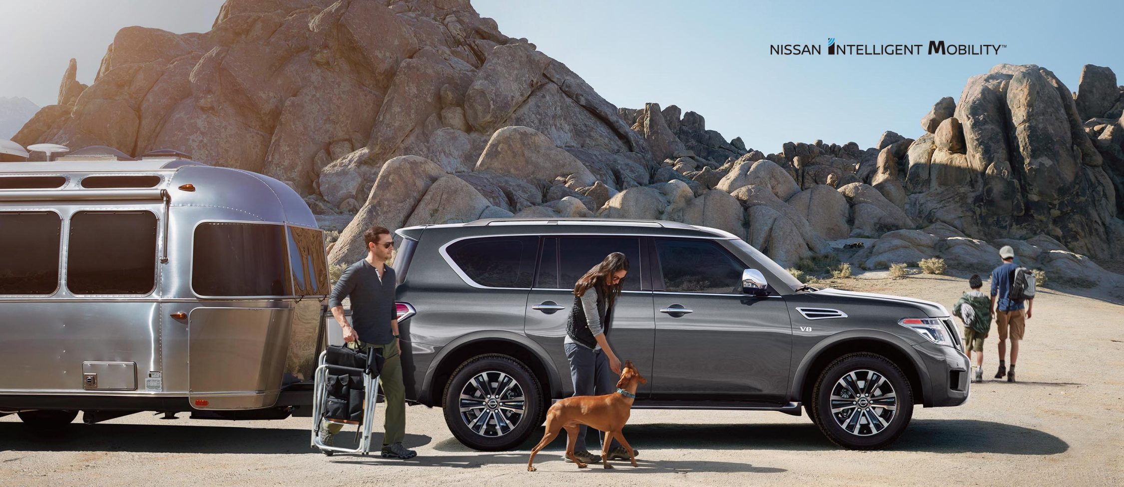 A gray 2020 Nissan Armada parked near the desert with a family and dog.