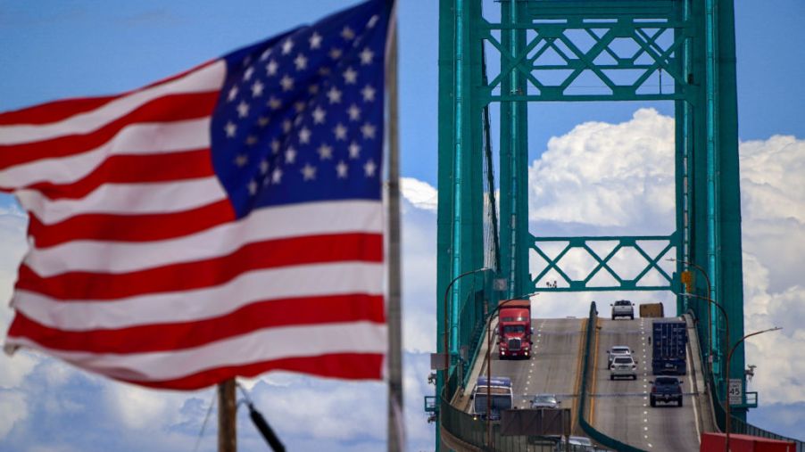 An American flag waves as cars and trucks go over a bridge.