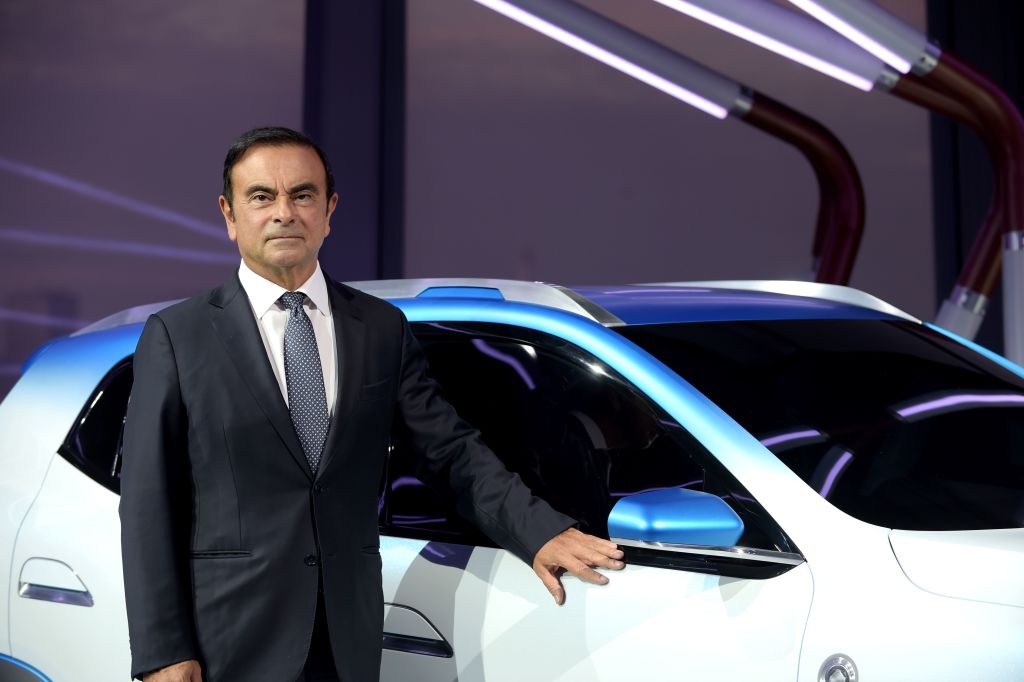 Former Nissan CEO Carlos Ghosn standing next to white Nissan crossover