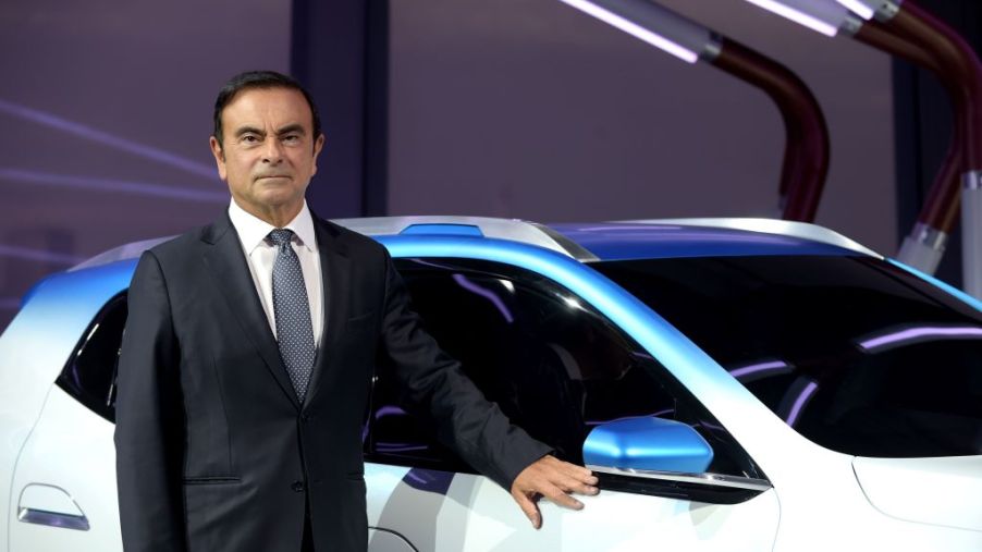 Former Nissan CEO Carlos Ghosn standing next to white Nissan crossover