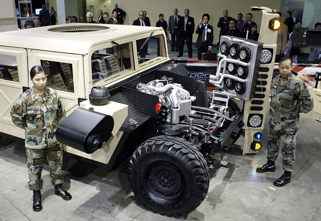 Two soldiers standing next to a military Humvee built by GM