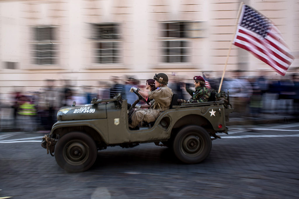 A military Jeep drives down the street with an American flag