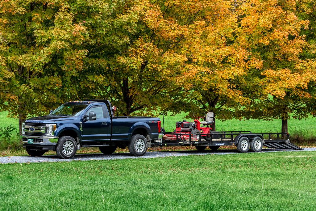 A lawn care service truck towing a lawn mower