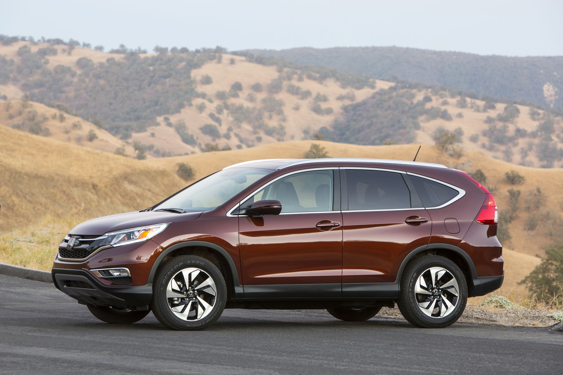 The 2015 Honda CR-V compact SUV model with a dark reed paint color option parked on an asphalt road near hills of yellow grass