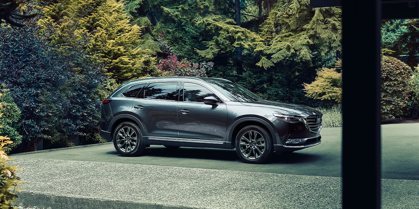 A grey 2020 Mazda CX-9 sparked in near a lush green forest.
