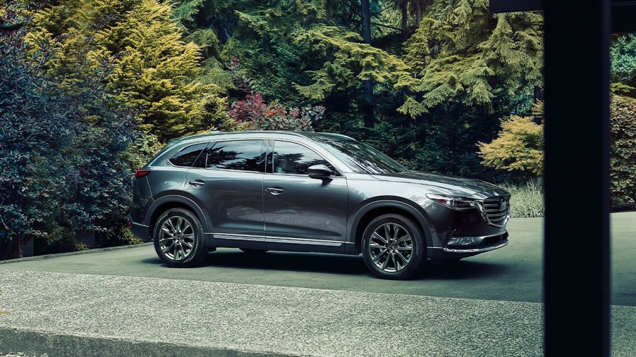 A grey 2020 Mazda CX-9 sparked in near a lush green forest.