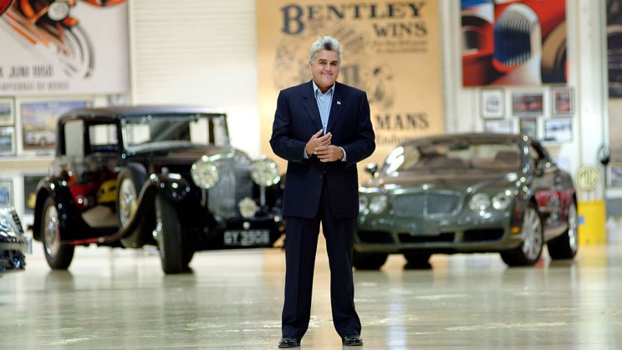 Jay Leno stands in front of 2 of his cars