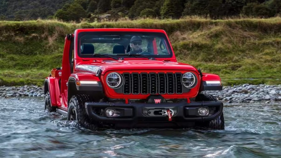 A red Jeep Wrangler small SUV is driving through water.