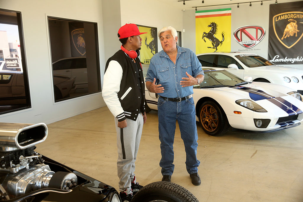 Jay Leno and Nick Cannon standing in a garage talking about cars