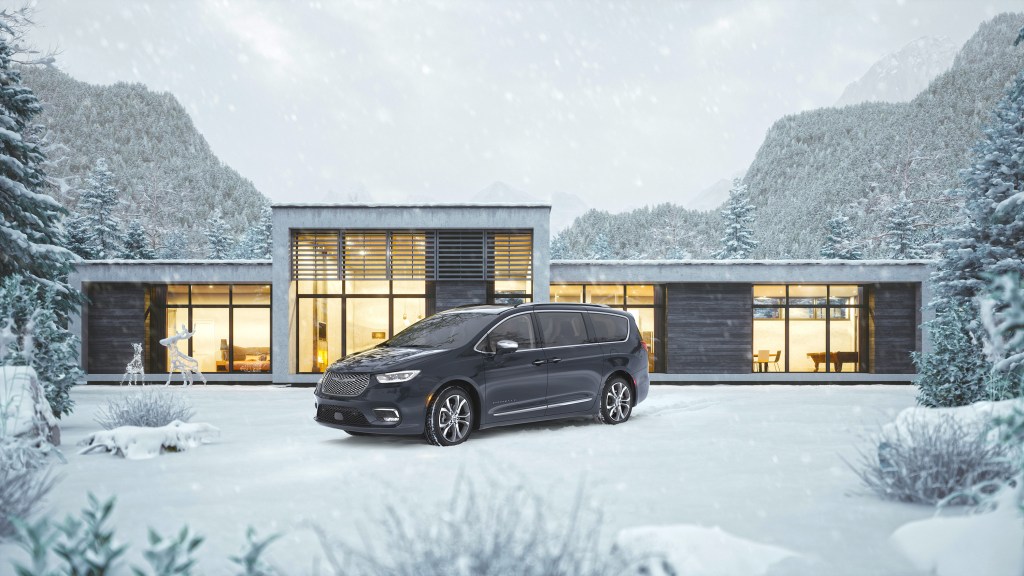 a refined looking black Pacifica in front of a modern home in the snow