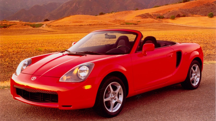 A red Toyota MR2 Spyder parked next to a picturesque countryside.