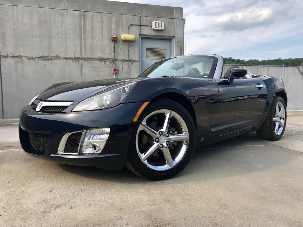 A black 2008 Saturn Sky roadster is parked in an industrial area.