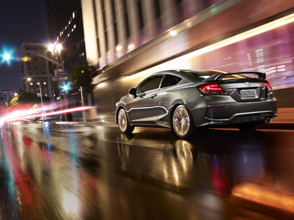 A silver 2015 Honda Civic Si Coupe driving down a wet urban highway.