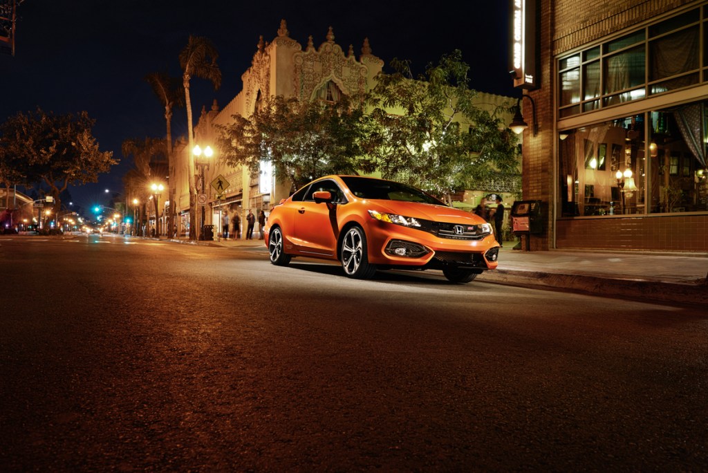 An orange 2015 Honda Civic Si Coupe parked on a city street at night.